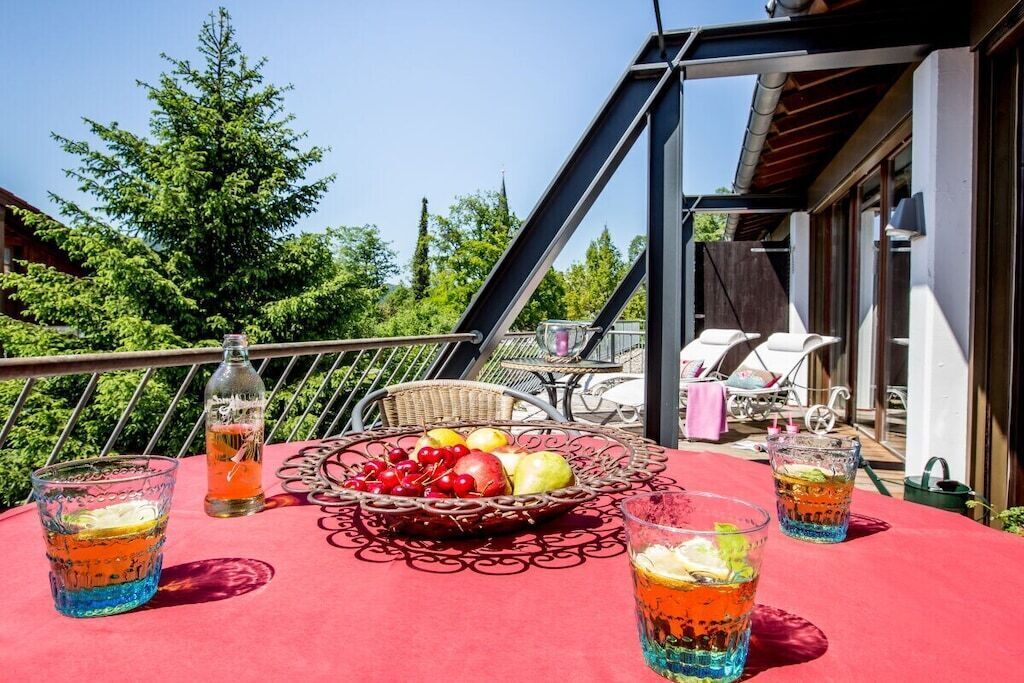 A balcony with a table set for a meal, a wicker basket with fruit, and two glasses of a beverage.