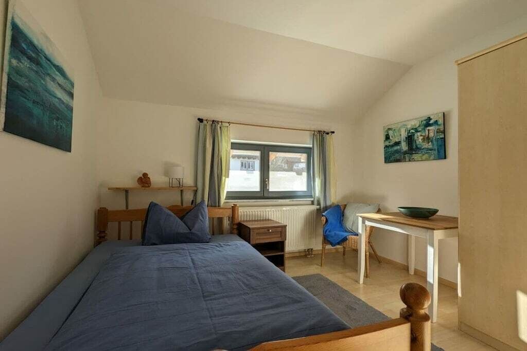 A bedroom with a bed, a desk, a chair, and a window with curtains.