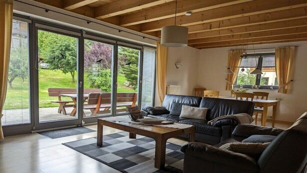 A living room with a sofa, coffee table, and a view of a garden through large sliding glass doors. - Ketterer Hinterzarten Black Forest (Hinterzarten)