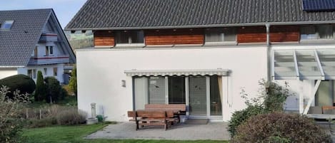 A modern two-story house with a sloped roof, large windows, and a solar panel on the roof.