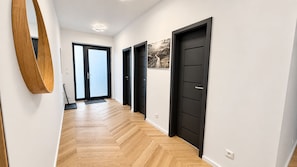 Un pasillo con piso de madera, puertas negras y un espejo grande.