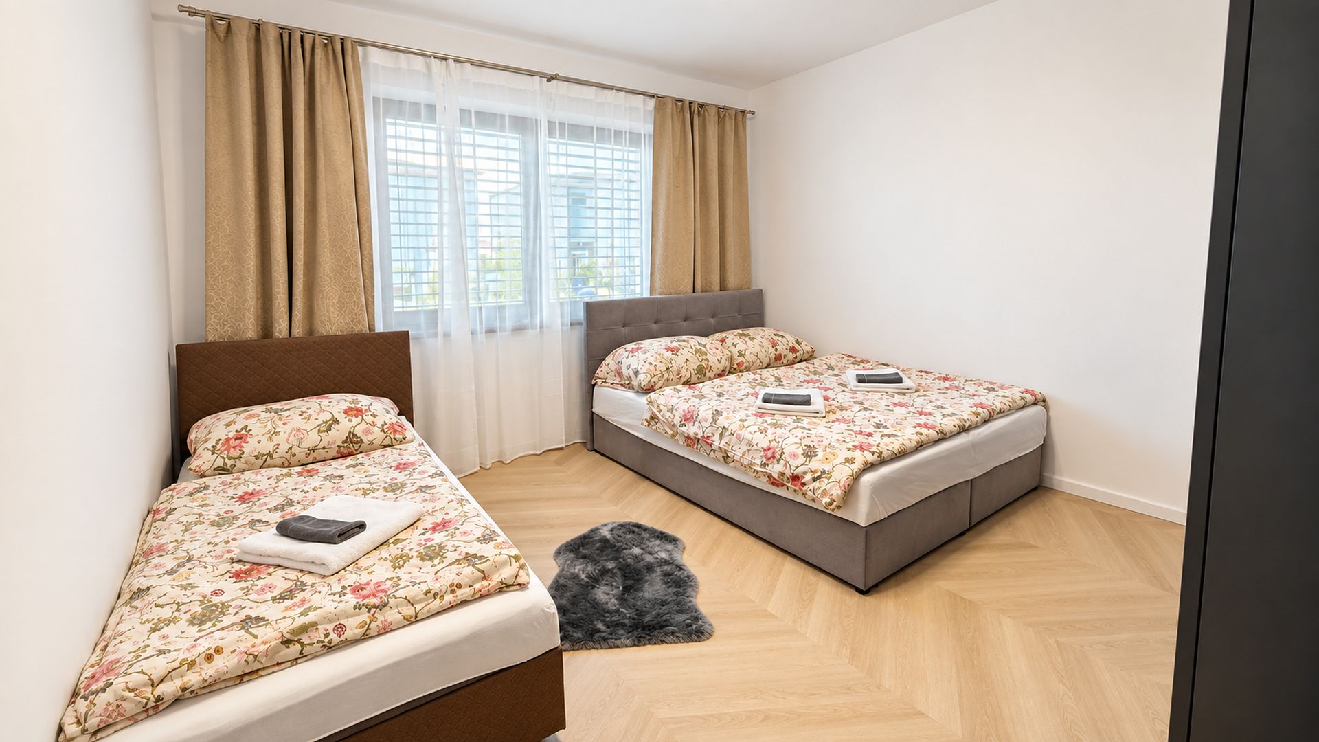 Une chambre avec deux lits, une fenêtre avec des stores et un petit tapis.