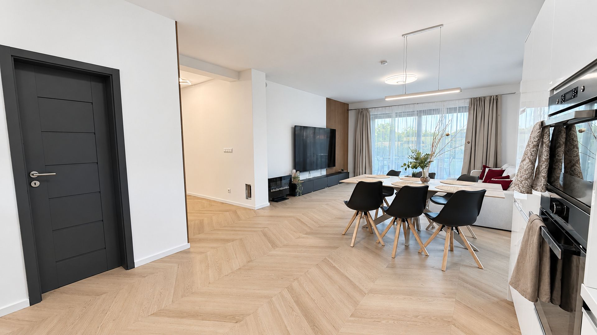 A modern living space with a dining area, kitchen, and a large window providing natural light.