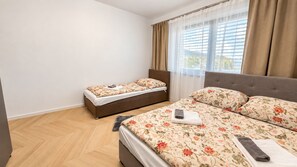 Un dormitorio con dos camas, un ventanal con cortinas y vistas al exterior.