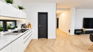 Cozinha moderna com armários brancos, porta preta e piso de madeira em padrão herringbone.