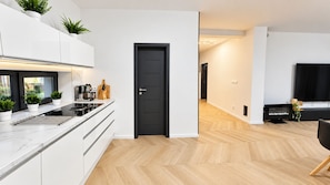 Una cucina moderna con mobili bianchi, una porta nera e un pavimento in legno a spina di pesce.