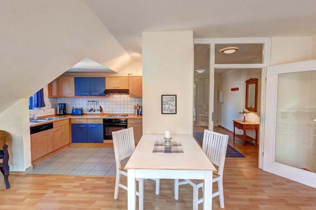 A compact kitchen with blue cabinets, a dining table with chairs, and a view into the living area.
