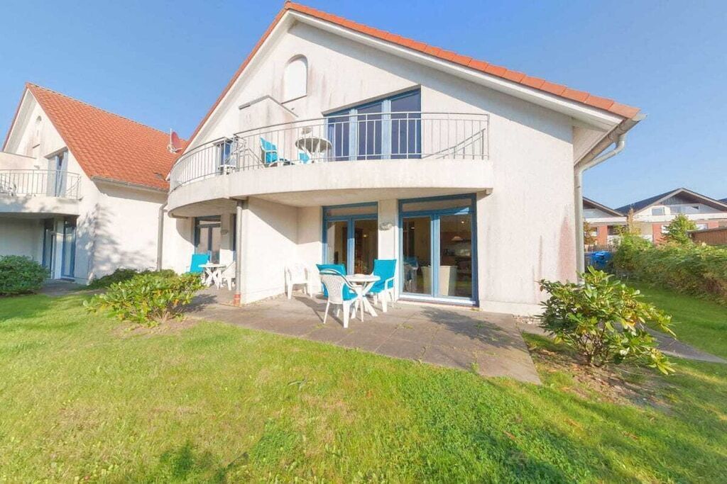 A two-story house with a balcony, a patio with outdoor furniture, and a well-maintained lawn.