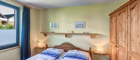 A bedroom with a double bed, two bedside tables with lamps, a wardrobe, and two wall-mounted picture frames.