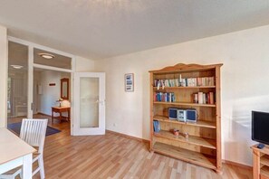 Een kamer met een houten boekenkast, een televisie en een eethoek met een tafel en stoelen.