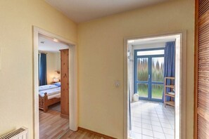 Een gang die leidt naar een slaapkamer met een houten deur en uitzicht op een balkon.