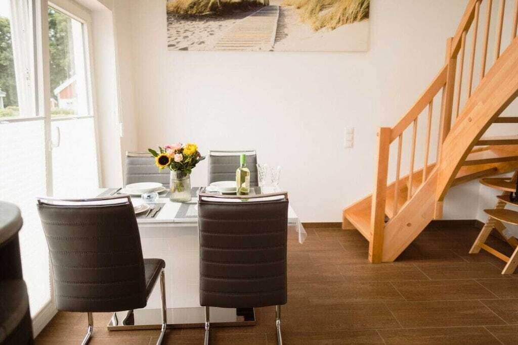 Un coin repas avec une table dressée pour deux personnes, deux chaises, un vase avec des fleurs et un escalier en bois.