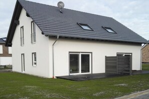 A modern two-story house with a sloped roof, large sliding glass doors, and a small attached garage. - Semi-detached house "LEE" (Butjadingen)