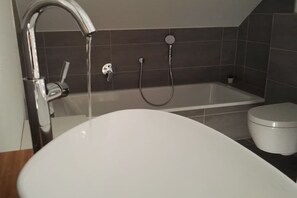 A modern bathroom with a white bathtub, a toilet, and a shower area. - Semi-detached house "LEE" (Butjadingen)