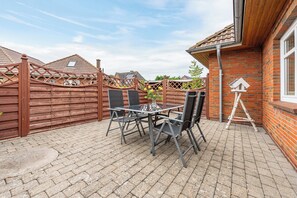 Une terrasse avec une table et des chaises, une clôture en bois et un mur en briques.