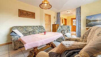 Un salon comprenant un canapé, des fauteuils, une table basse, un meuble en bois et un téléviseur.
