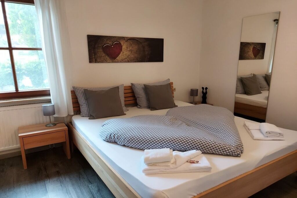 Quarto com uma cama grande, mesa de cabeceira, espelho e janela.
