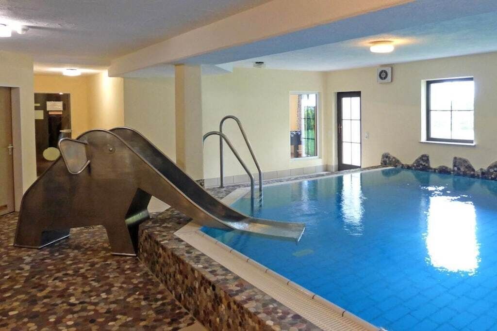 Une piscine intérieure avec un toboggan, un sol carrelé et une fenêtre laissant entrer la lumière naturelle.