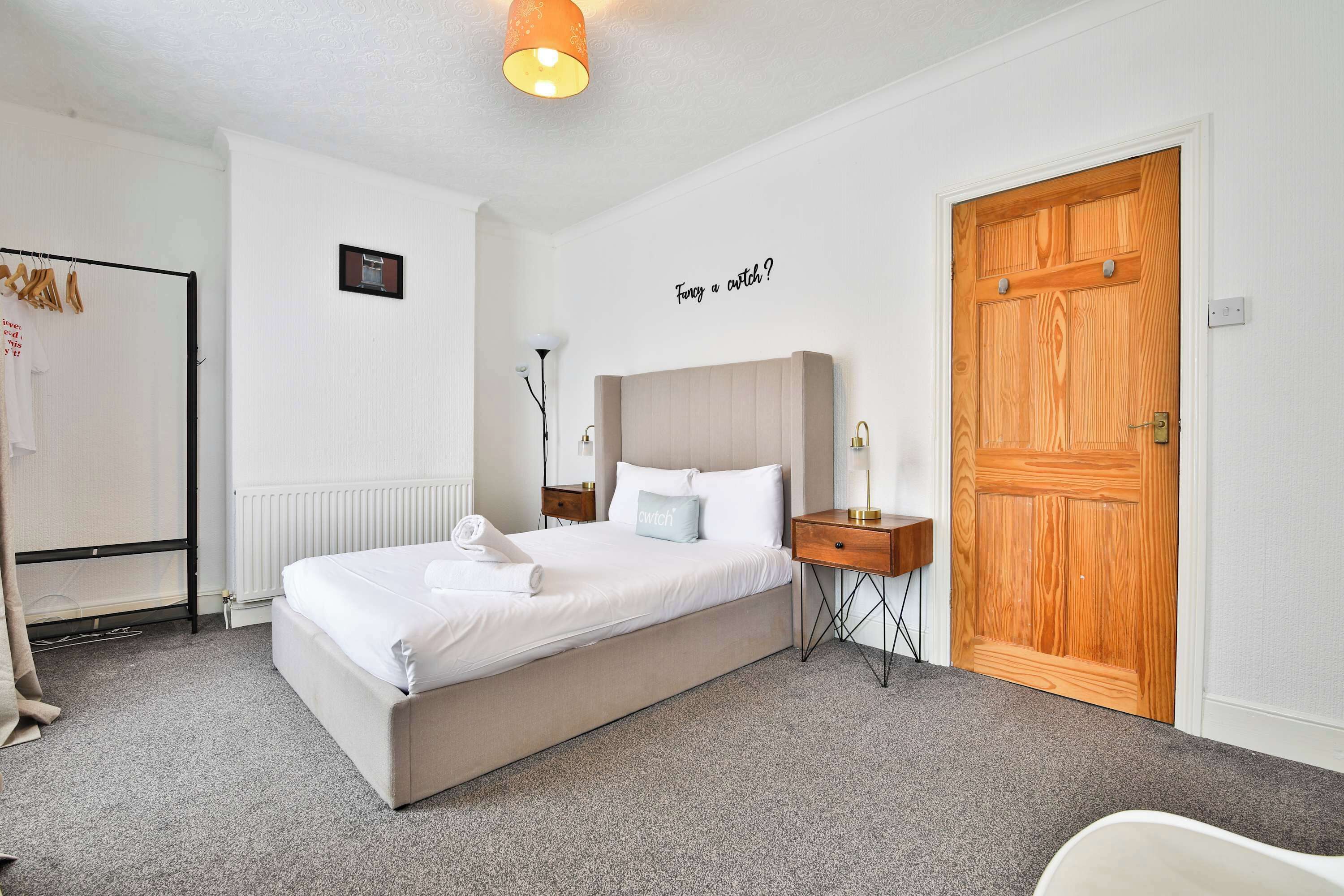 A neatly arranged bedroom with a bed, a bedside table, a wardrobe, and a wall-mounted light fixture.