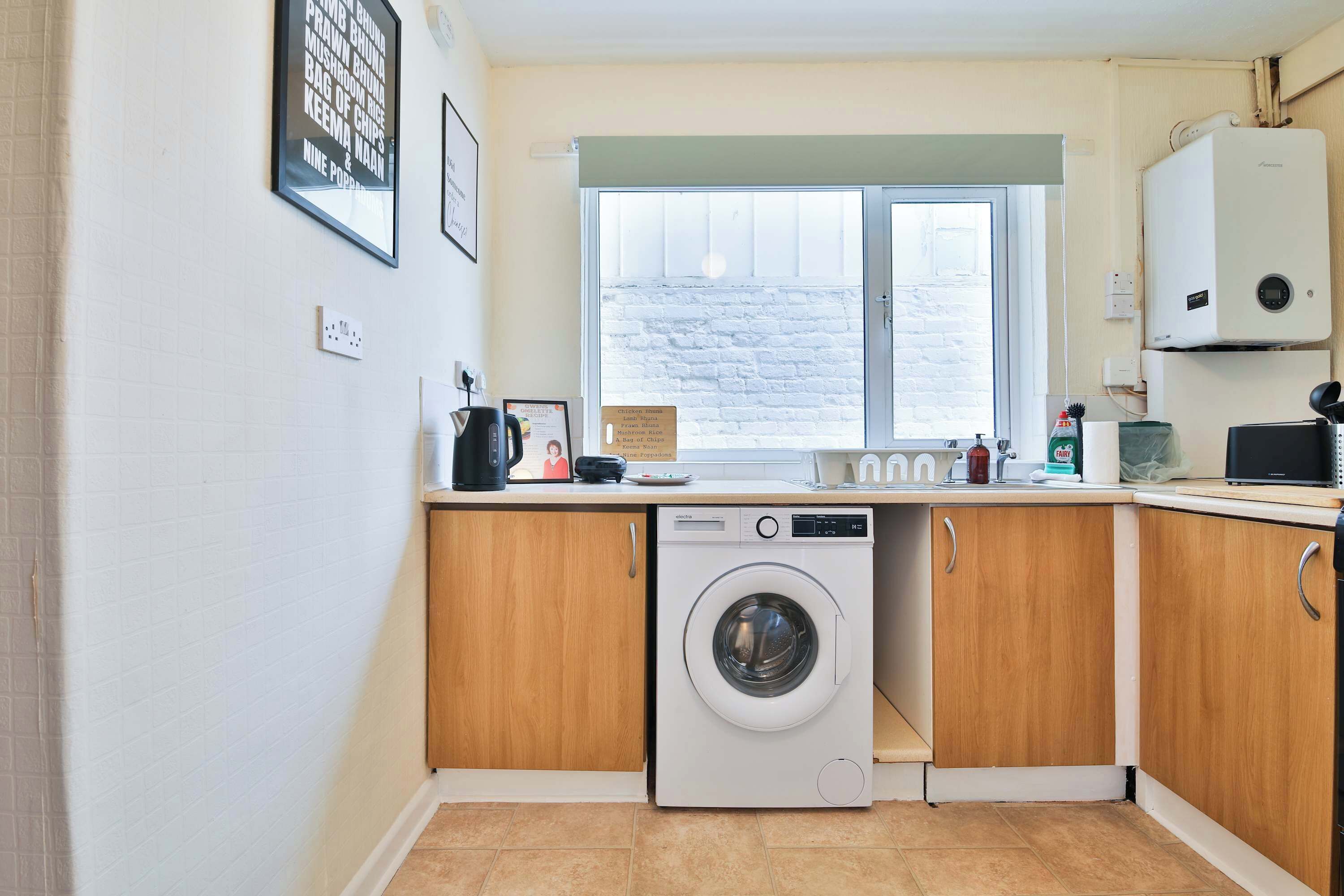 A compact kitchen with a washing machine, a window, and a view of a brick wall outside.