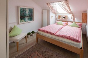 A bedroom with a bed, a bench, a small table, and a wall-mounted shelf.