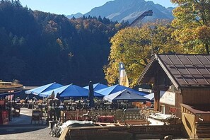 A mountain-side outdoor seating area with blue umbrellas, wooden tables, and chairs.