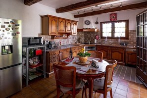 A kitchen with wooden cabinets, a stainless steel refrigerator, a dining table with chairs, and a window with curtains. - Villa in Vence with swimming pool (Vence)