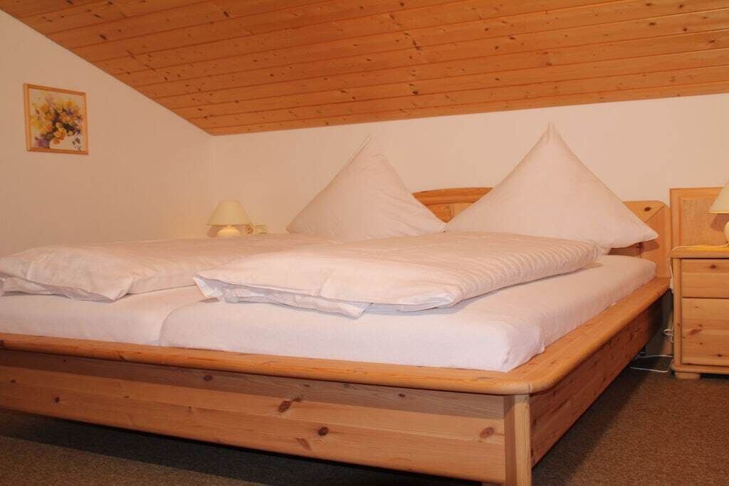 Ein hölzernes Bett in einem Raum mit schrägem Dach und einem Nachttisch mit Lampe.