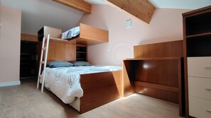 Een stapelbed met een ladder, een kledingkast en een bureau in een kamer met houten balken aan het plafond.