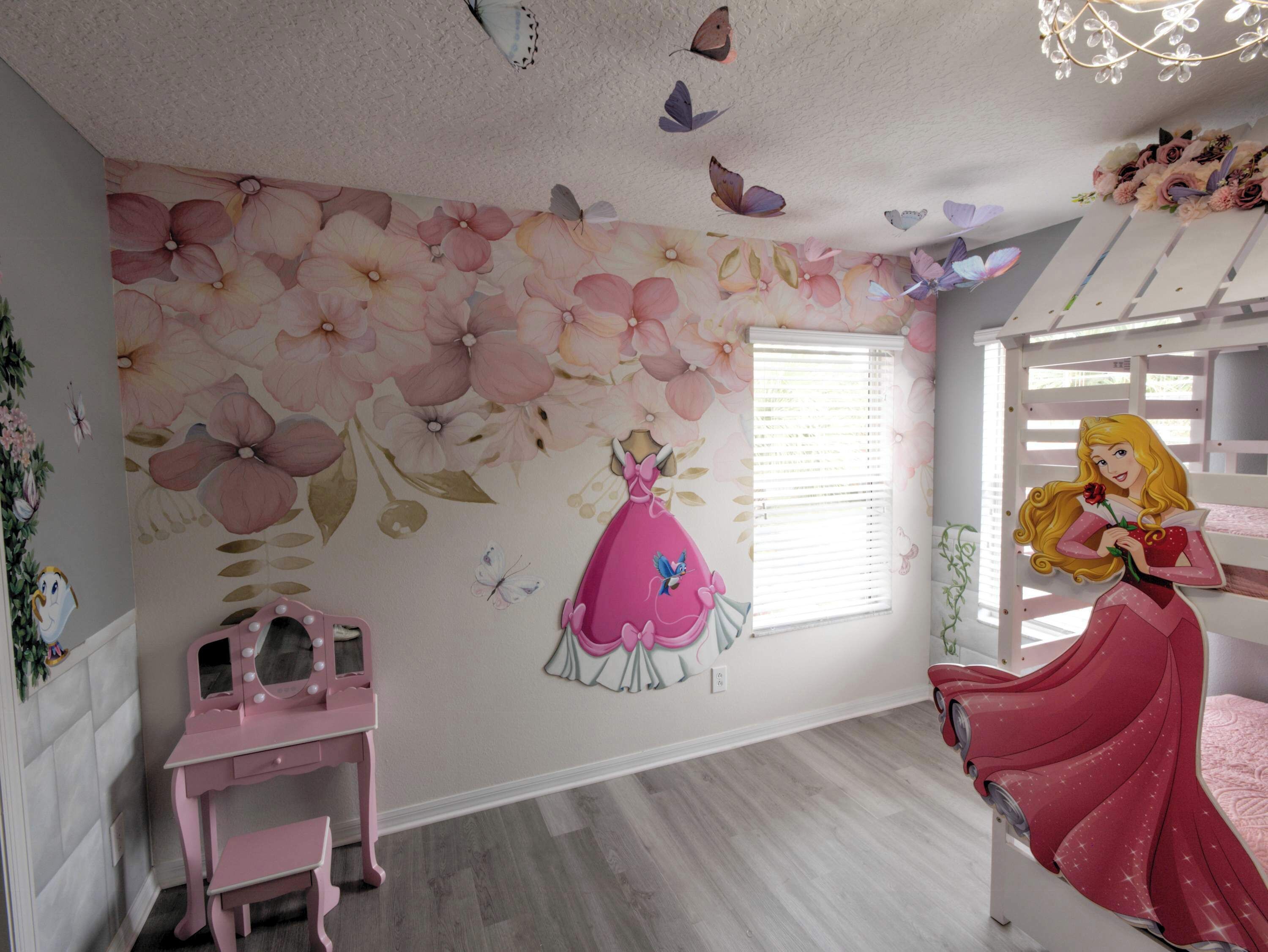 Een kamer met een bloemenmuur, een roze bureau, een stapelbed met een sprei met prinsessenthema en vlinders aan het plafond.