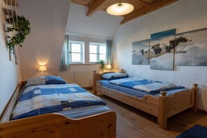 Una habitación con dos camas de madera, un ventanal con cortinas y una lámpara fijada a la pared.