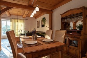 Un comedor con una mesa de madera dispuesta para cuatro, una lámpara colgante y un armario de madera con cristalería.