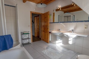 Un baño con bañera, dos lavamanos y una puerta de madera que da a otra habitación.