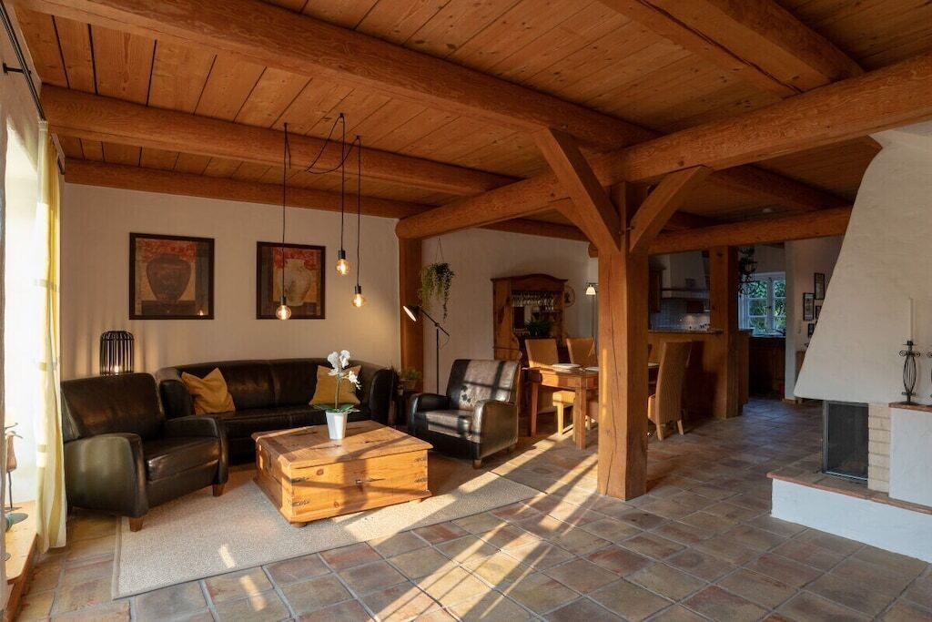 A spacious living area with a wooden ceiling, a black leather sofa, a wooden coffee table, and a fireplace.