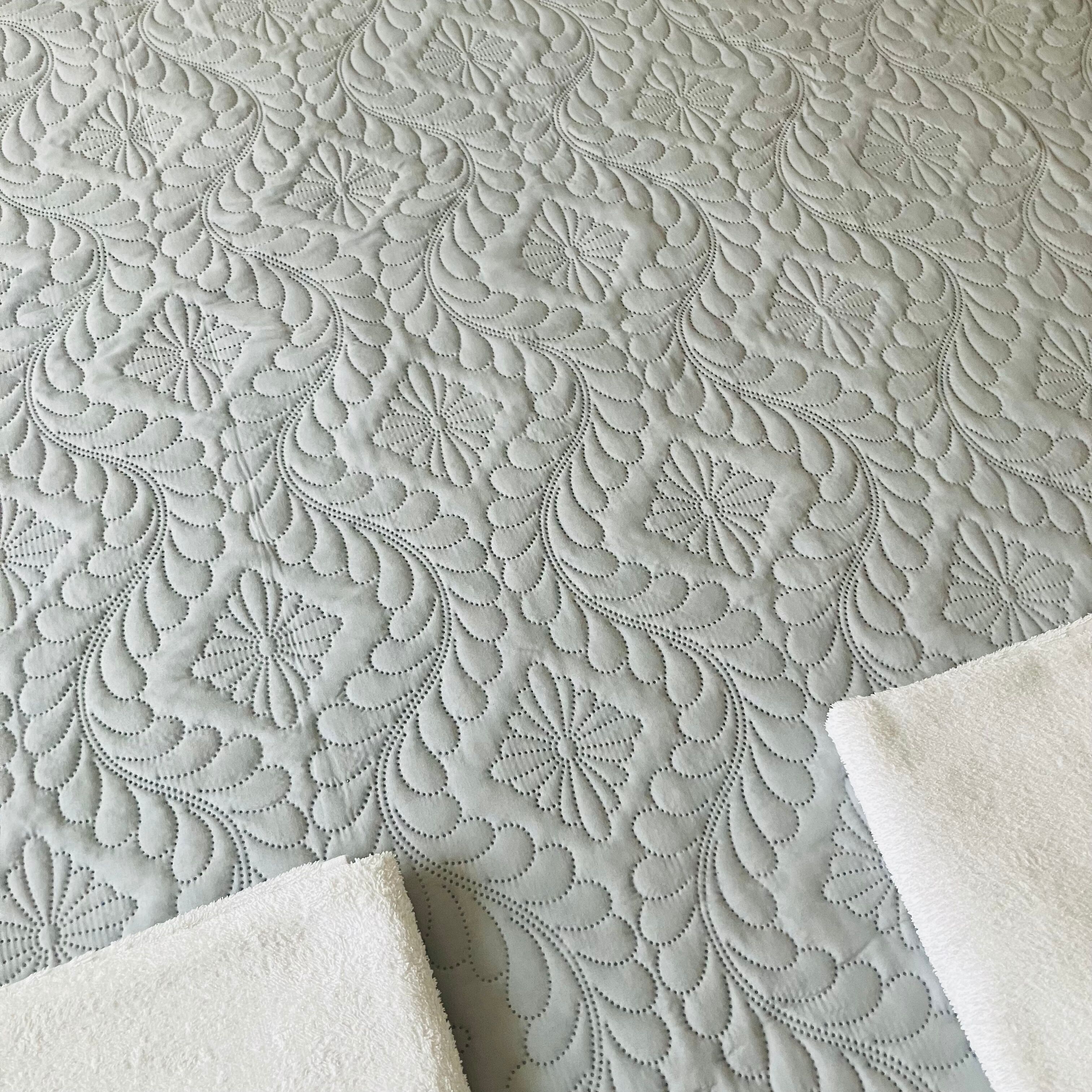 Un tissu à texture particulière, orné d’un motif floral, probablement utilisé pour un lit ou un meuble rembourré.