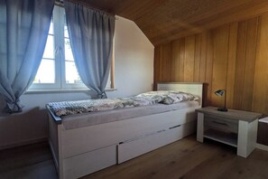 Un dormitorio con una cama, una mesita de noche, una ventana con cortinas y paredes de madera.