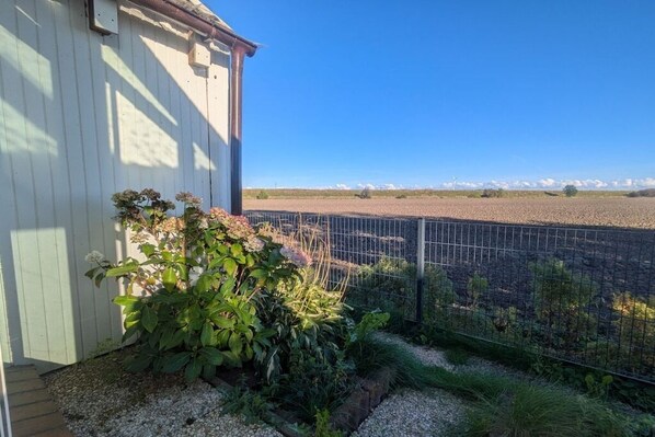 Un jardín cercado con un edificio a un lado y vistas a un campo y montañas a lo lejos.