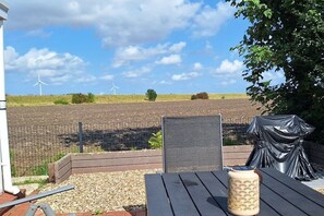 Un patio con una mesa, una silla y un jarrón decorativo. Al fondo, se ven aerogeneradores y una zona delimitada por una valla.
