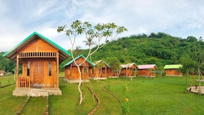Uma fileira de cabanas de madeira com telhados verdes, rodeadas por vegetação exuberante e uma paisagem montanhosa ao fundo.