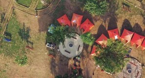 An aerial view of a circular building with a central courtyard, surrounded by red umbrellas, and trees.