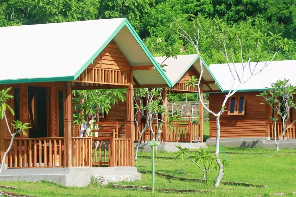 A row of wooden cabins with a porch and a grassy area in front.