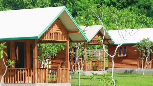 A row of wooden cabins with a porch and a grassy area in front.