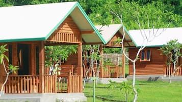 A row of wooden cabins with a porch and a grassy area in front.