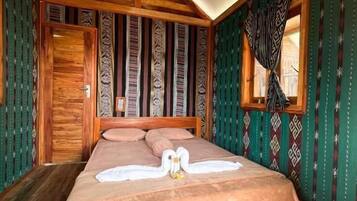 Una habitación con una cama, vigas de madera en el techo, una ventana con cortinas estampadas y una puerta.