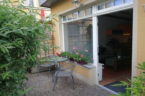 Un patio con mesa y sillas, una ventana con persianas y una puerta que da a un espacio interior.
