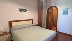 Een slaapkamer met een enkel bed, een nachtkastje, een lamp, een wandlamp, een houten deur en een klein schilderij aan de muur.