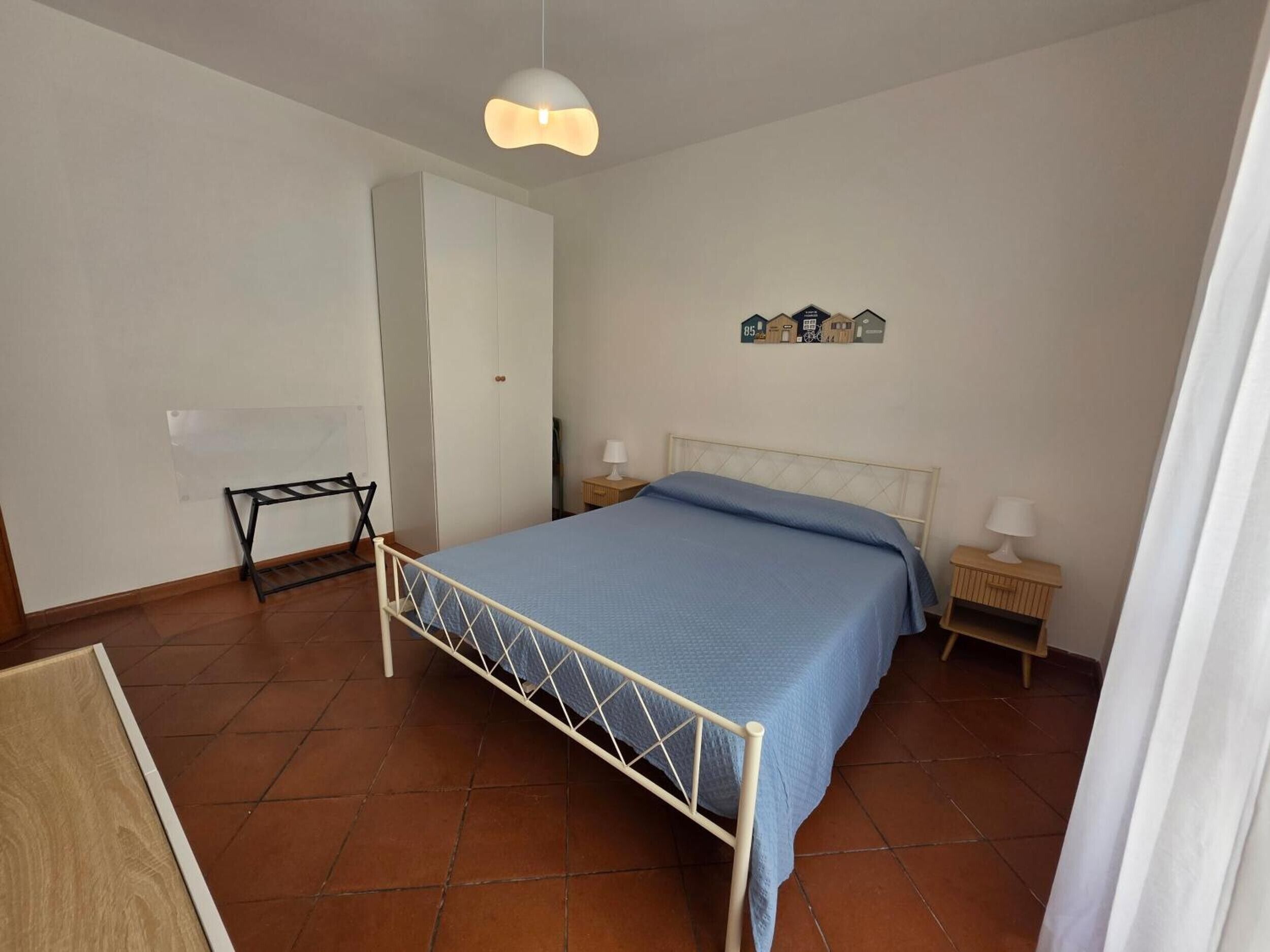 Ein Schlafzimmer mit einem Bett, Nachttischen, einer Hängelampe und einem Wandbild.