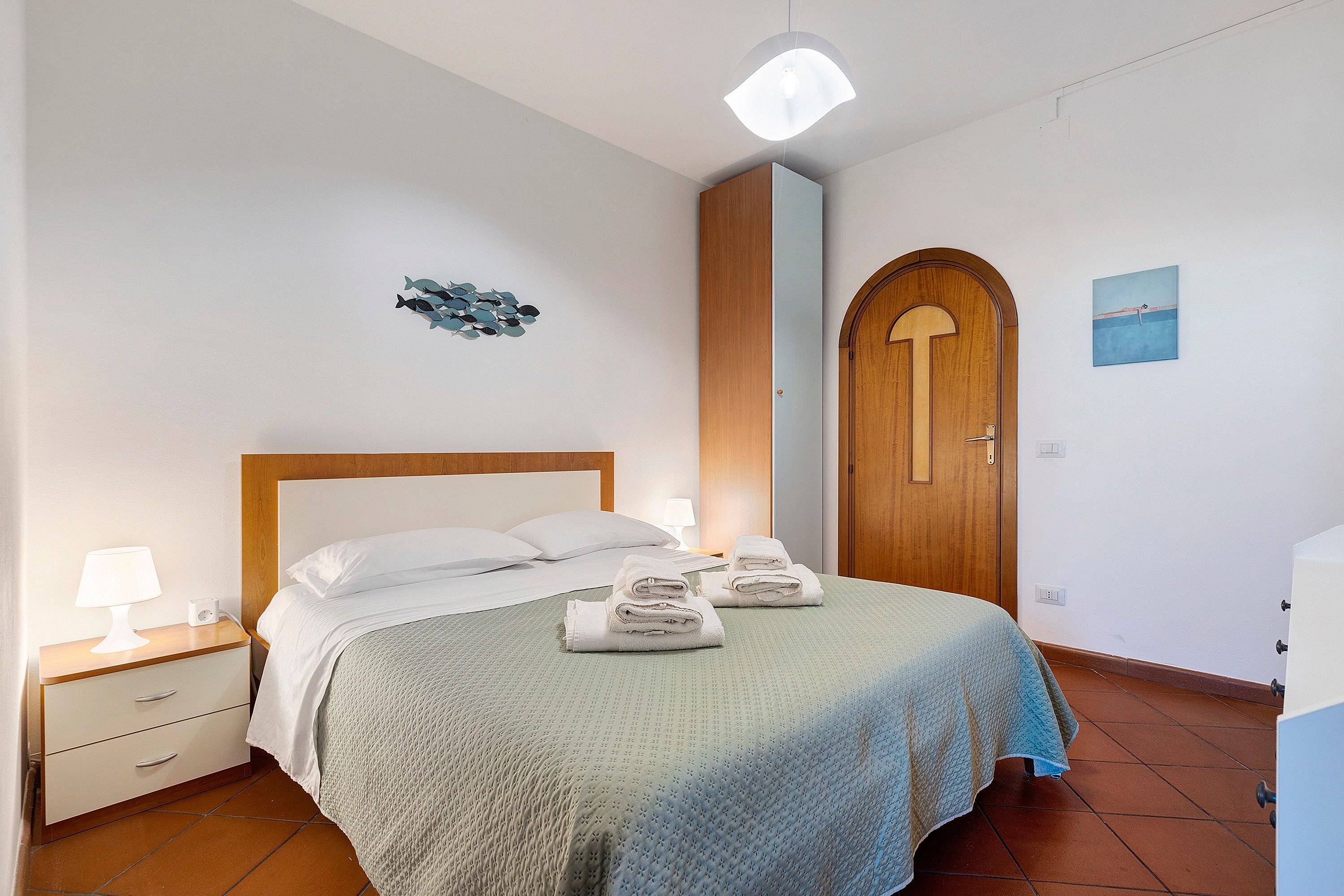 Une chambre d’hôtel avec un lit, une table de chevet, une lampe, une porte en bois et une œuvre d’art murale.
