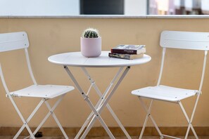 Une petite table ronde sur laquelle sont posés un cactus en pot et deux livres, et qui est flanquée de deux chaises blanches.
