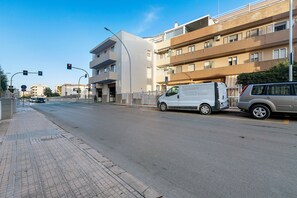 A street view with a white van parked on the side, a pedestrian crossing, and a multi-story building with balconies. - Apartment 'Bentu E Mare' with Sea View, Wi-Fi and Air Conditioning (Alghero)